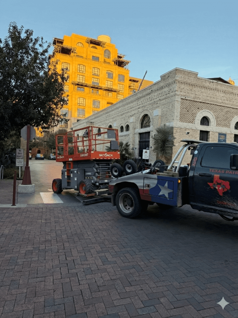 and orange Scissor Lift being towed by black truck of texas patriot towing