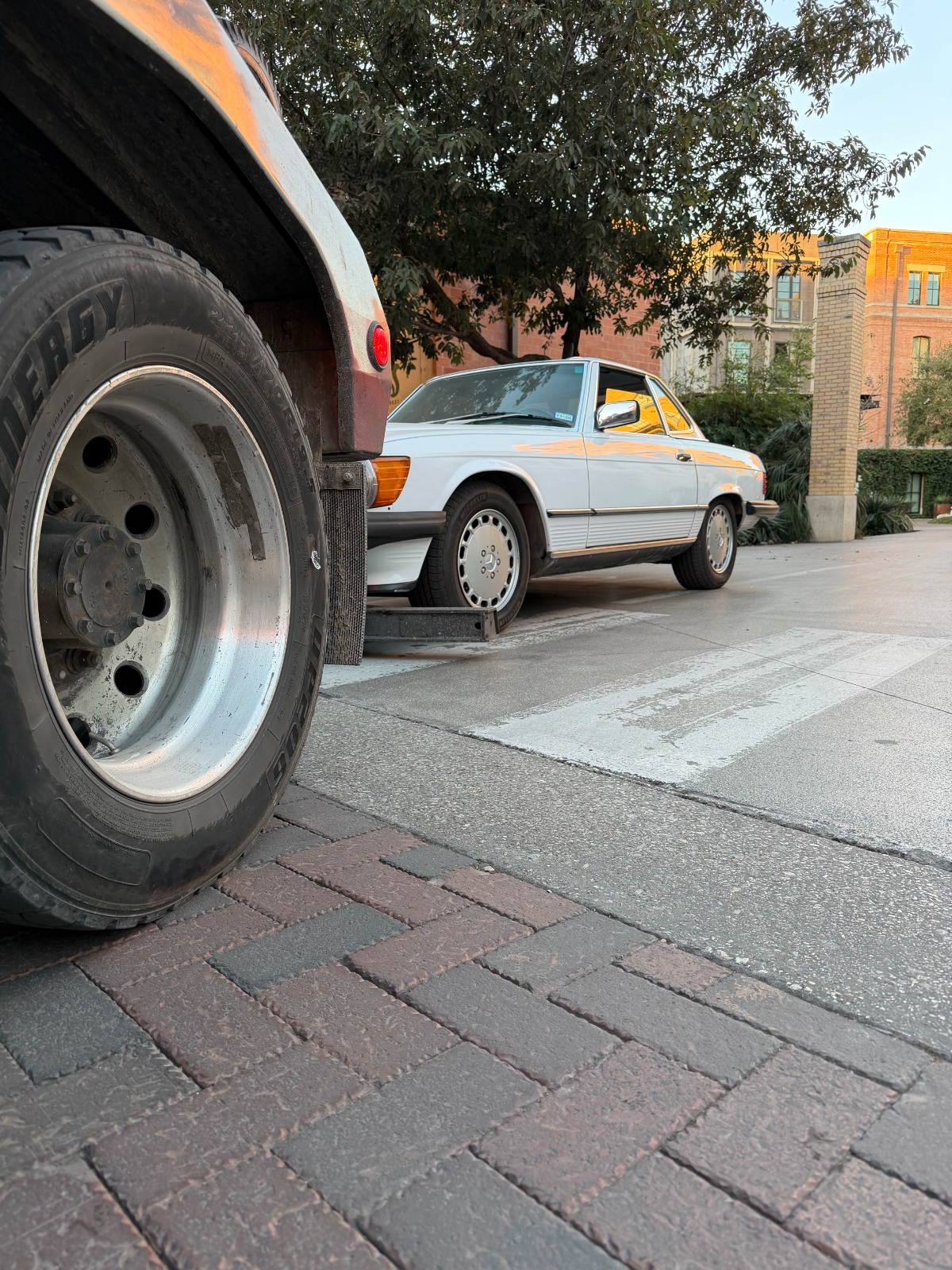 image of a white sedan being towed and the rear wheel of a tow truck in the image